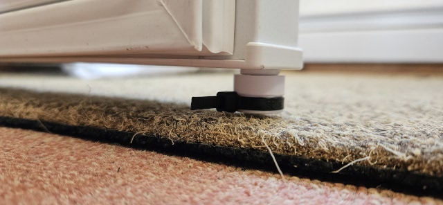 Freezer door which has a cable tie mounted on a post underneath. The door is open and a floor mat is immediately below the door.