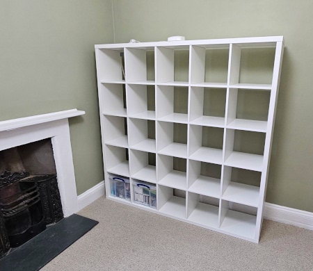 [White IKEA 5x5 KALLAX storage unit with a clear plastic box in the two leftmost positions of the bottom row and a white WiFi Access Point on the top]