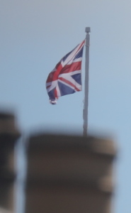 [Union Jack flag of the United Kingdom on the Royal Palace at Edinburgh Castle, visible above the chimney stack of a nearby building]