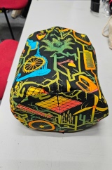 [Patterned fabric doorstop cover lying on its side showing the zip on the back and bottom, with the doorstop inside it]