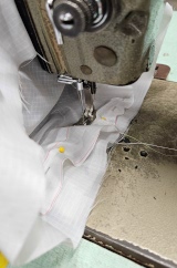 [White ripstop PVC cylinder on its side in a sewing machine to attach the top, sealing the inner waxed canvas with sand inside it]